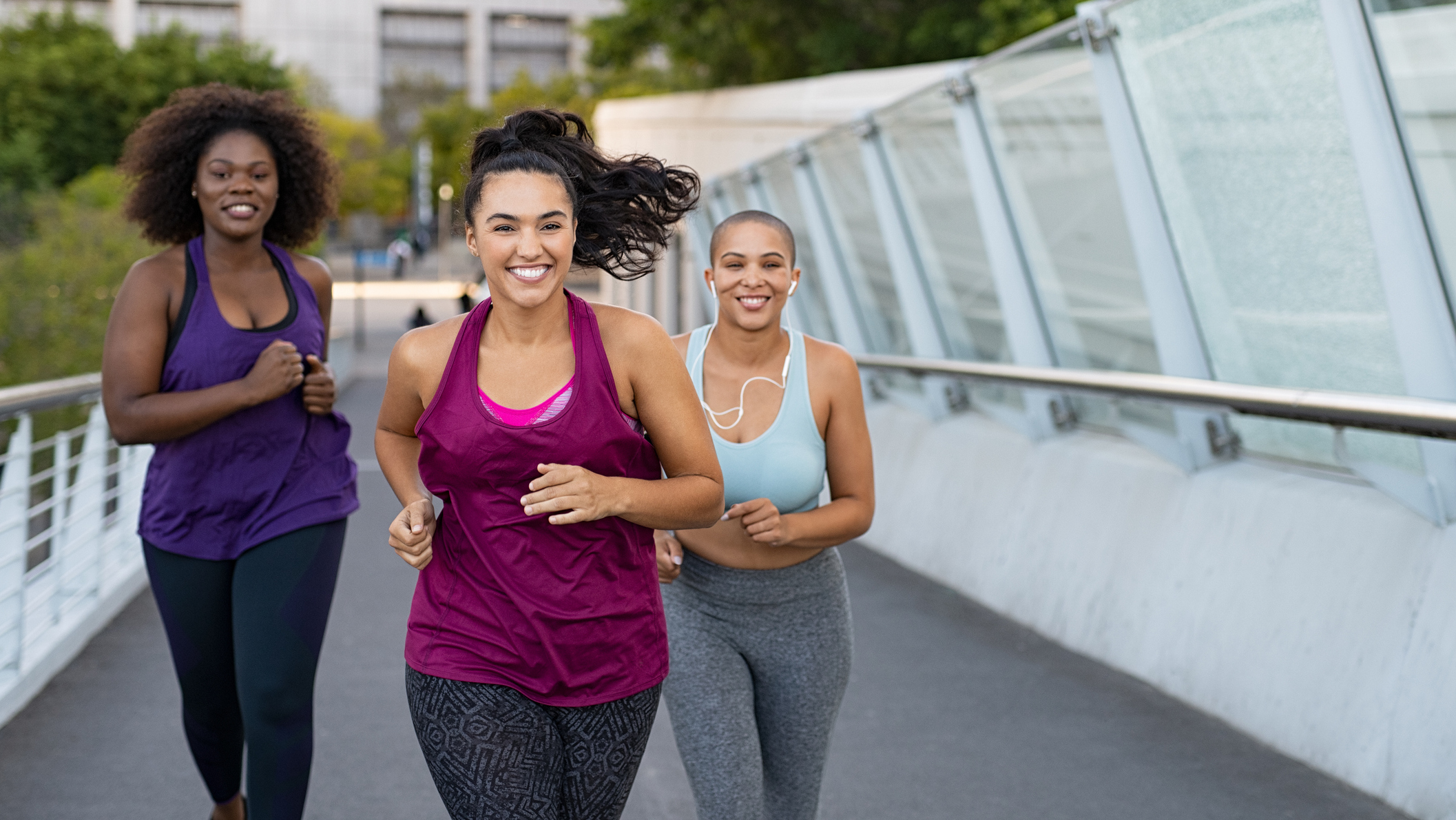 Three smiling women running on bridge in urban environment. They are all wearing leggings and tank tops.
