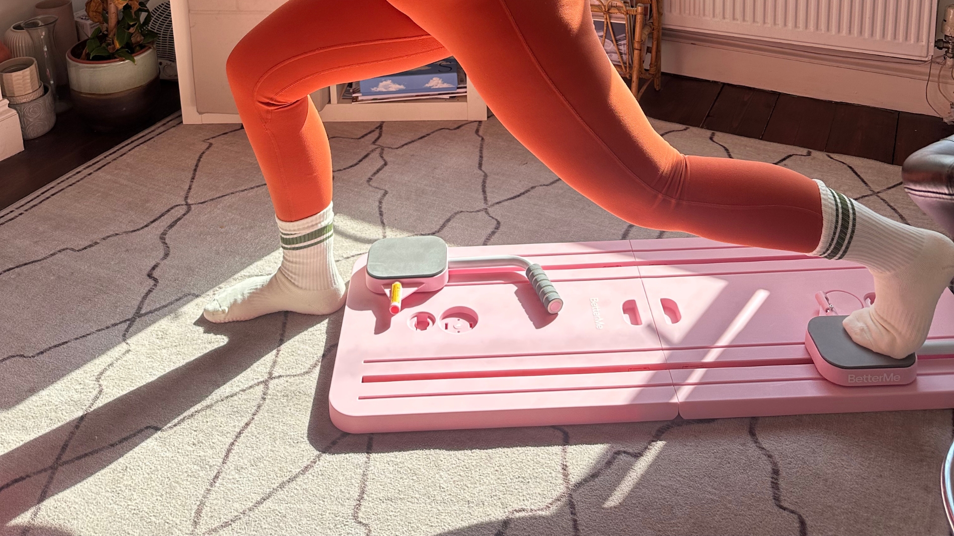 Bottom half of person exercising using a Pilates board, with one foot on a slider on the board and the foot behind the person’s front foot