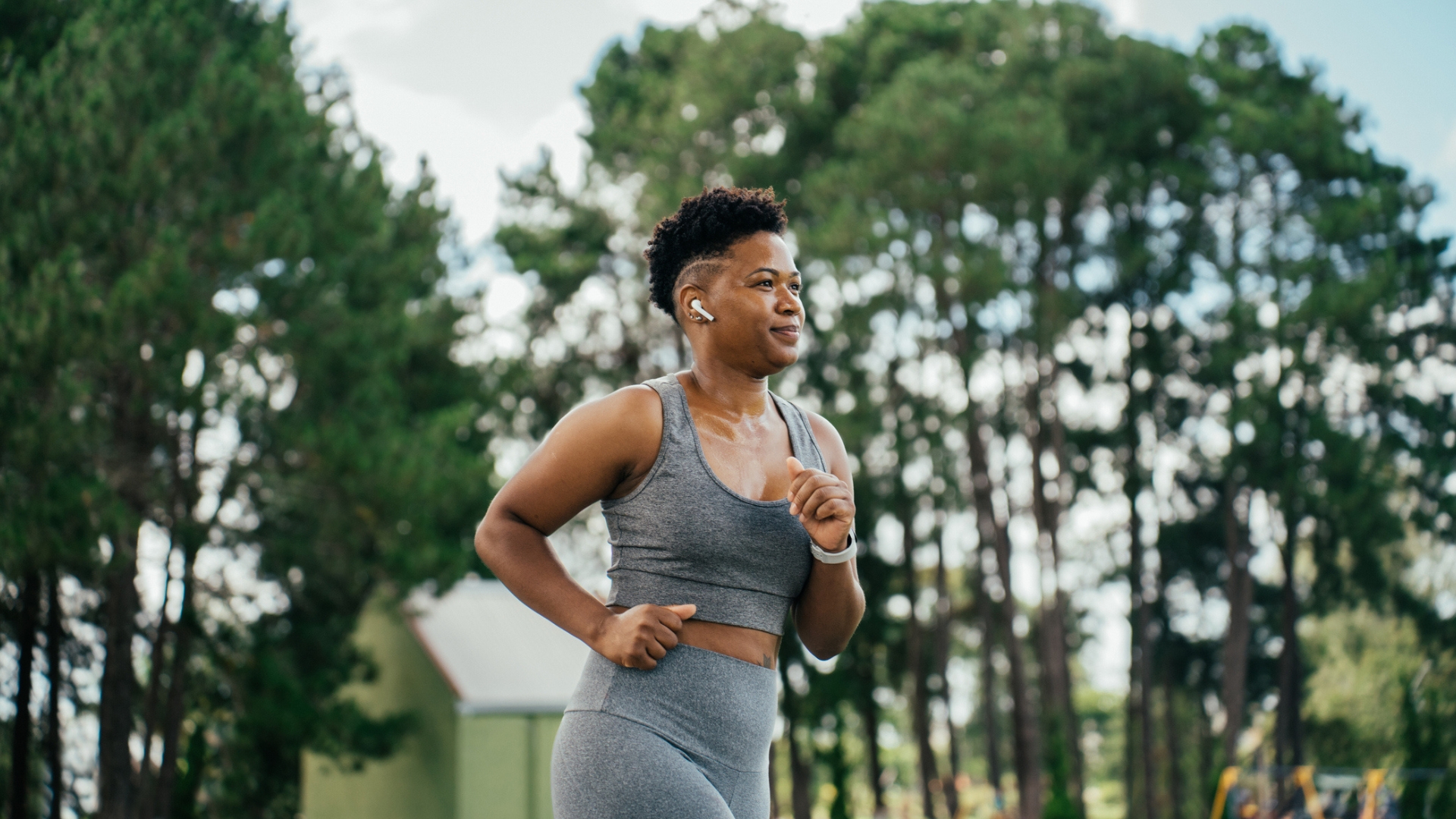 woman in a grey vest and leggings running outside with trees behind her. the shot is cropped at her hips with a side-on view.