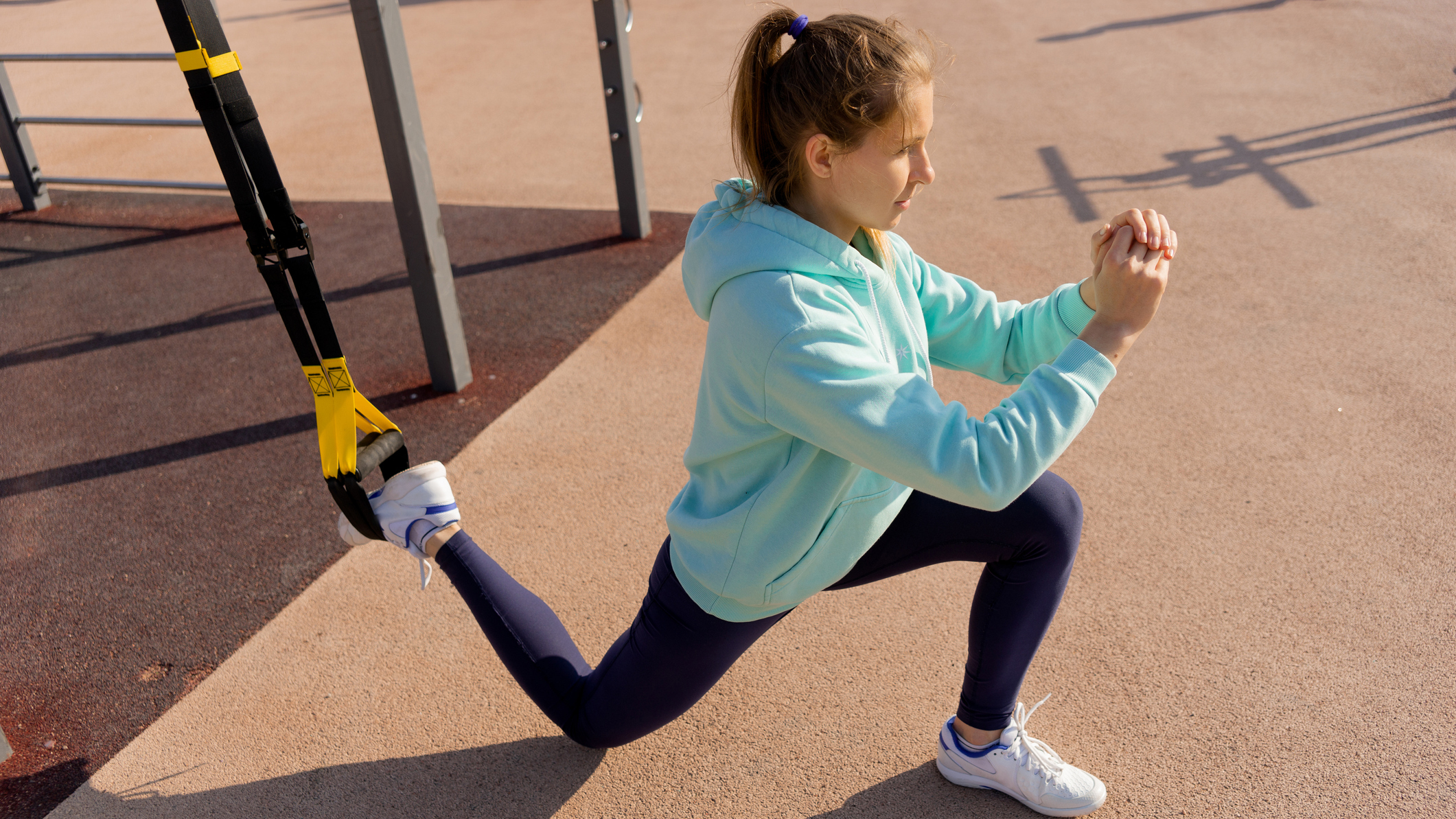 Woman performs a single-leg exercise using a TRX suspension trainer outside