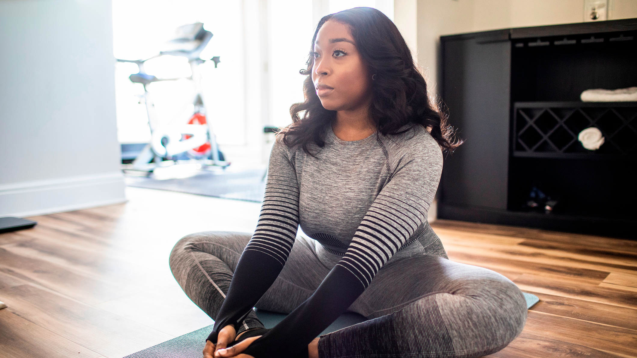 A woman wearing matching gym leggings and long-sleeve top sits on an exercise mat on the floor with the soles of her feet together and knees pointing out to the sides