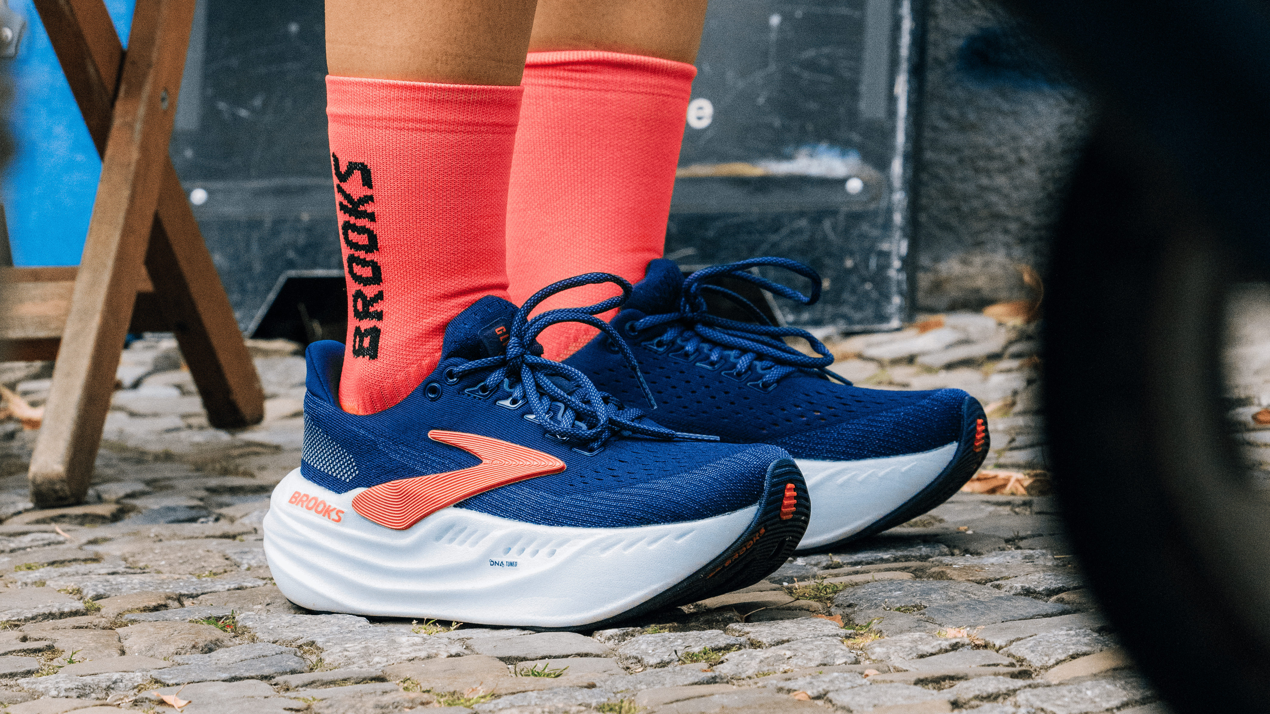 Person's feet seen wearing blue running shoes and pink socks with "Brooks" written down one side on a cobbled street